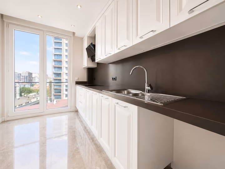 White kitchen cabinets, dark countertop and sink beside a full-height window.