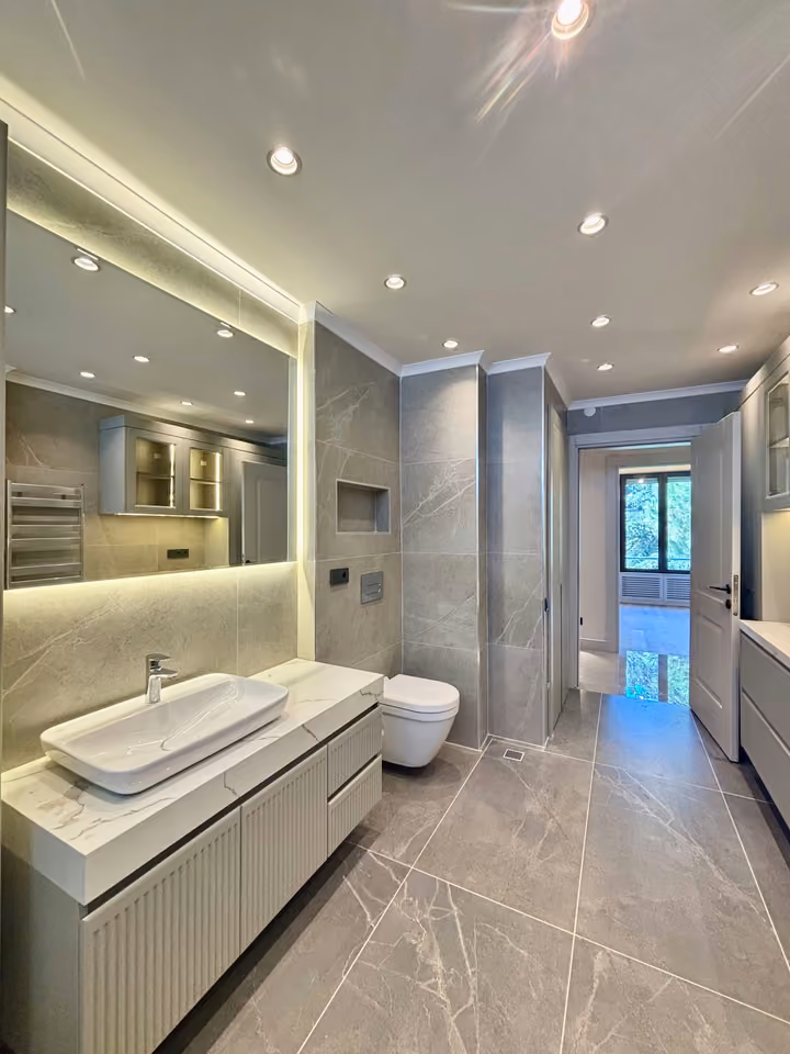 Bathroom with a countertop basin, illuminated mirror, wall-mounted toilet and storage.