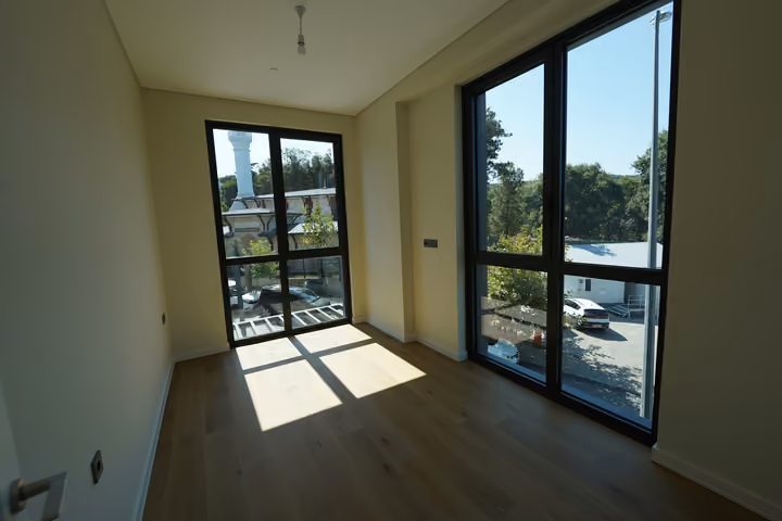 The bedroom viewed from the entrance, showing two window walls and wood flooring.
