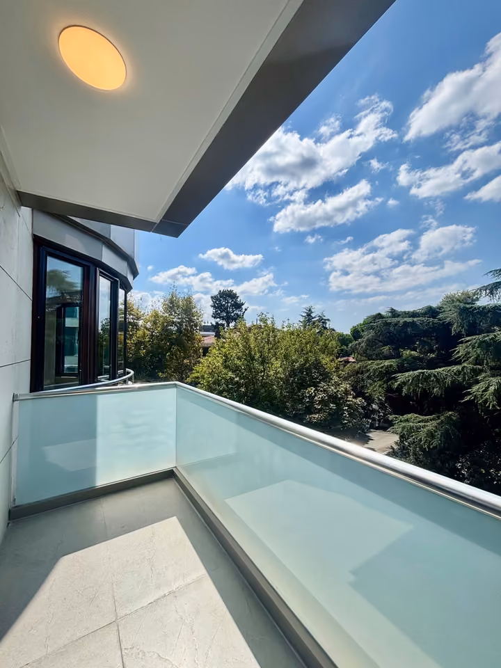 Balcony with frosted glass railing overlooking trees.