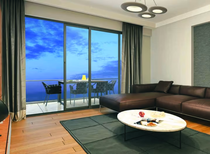 Interior visualization showing a corner sofa, coffee table and a glazed balcony with outdoor dining furniture.