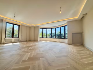 Wide living room with curved windows, herringbone-pattern flooring and recessed lighting.