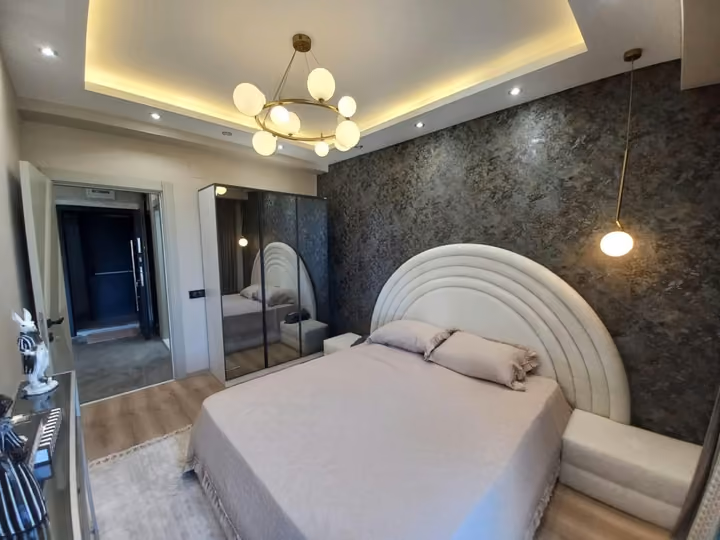 A furnished show apartment double bedroom with a padded headboard and mirrored wardrobe.