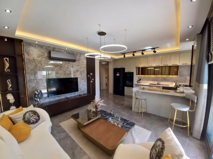 A furnished living room with a media wall, sofa and adjoining open kitchen.