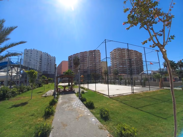 A landscaped path beside an outdoor sports court and neighboring buildings.