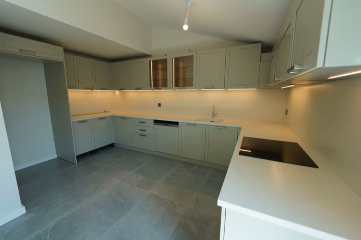 A fitted kitchen with pale cabinets, a light worktop, an electric hob and a tiled floor.