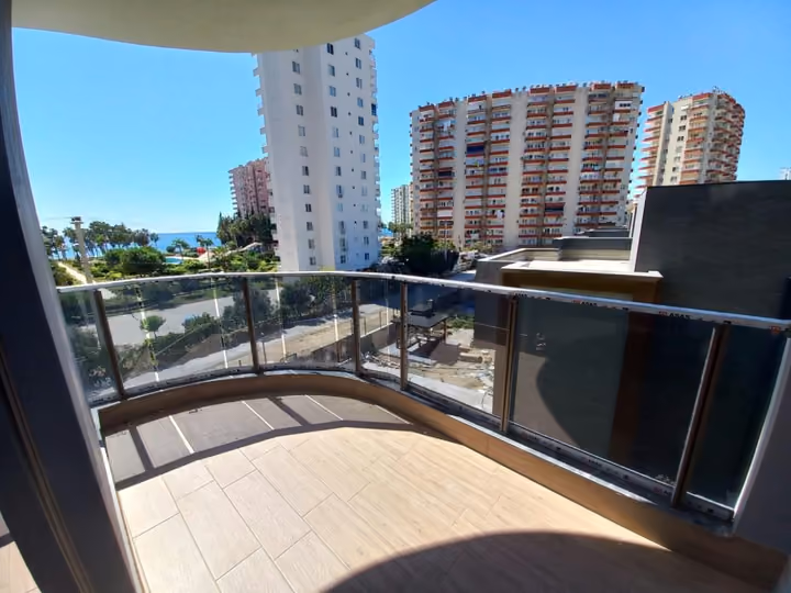 A photographed corner balcony with glass railings and nearby buildings in view.