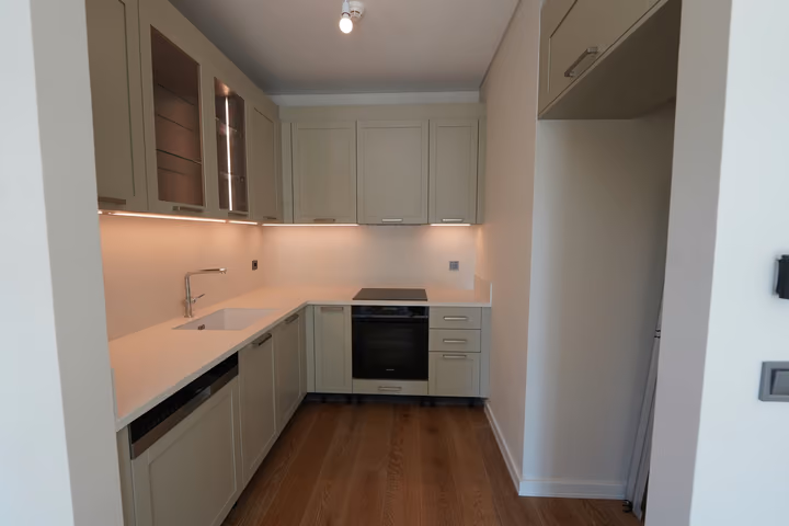The fitted kitchen viewed from its opening, with pale cabinetry and a continuous light worktop.