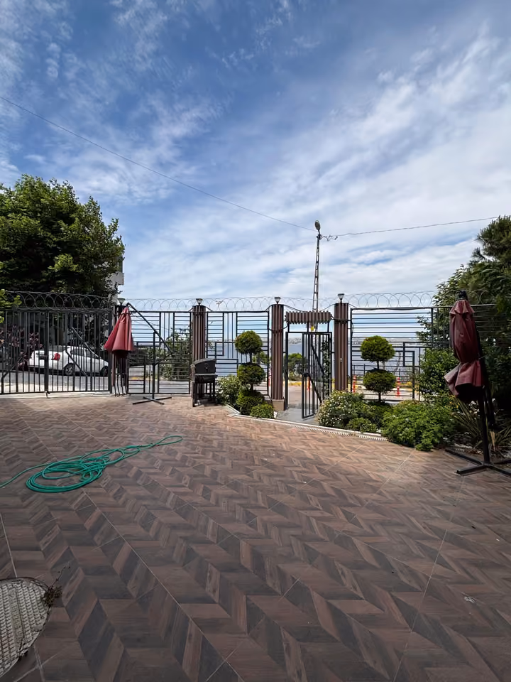 Paved courtyard with landscaping and sea views beyond the entrance.