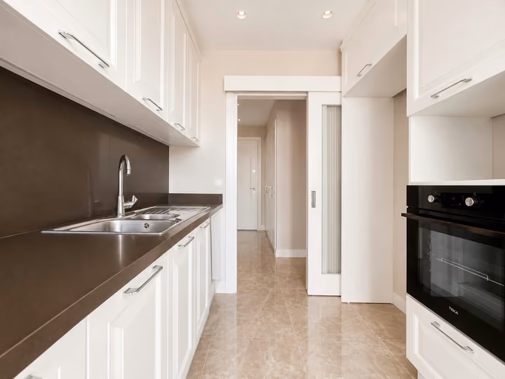White kitchen cabinets, built-in oven and sink with a view toward the hallway.