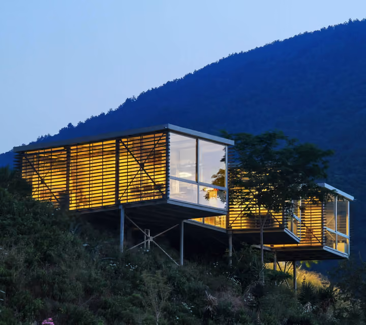 Elevated glazed pavilion on the hillside at dusk.