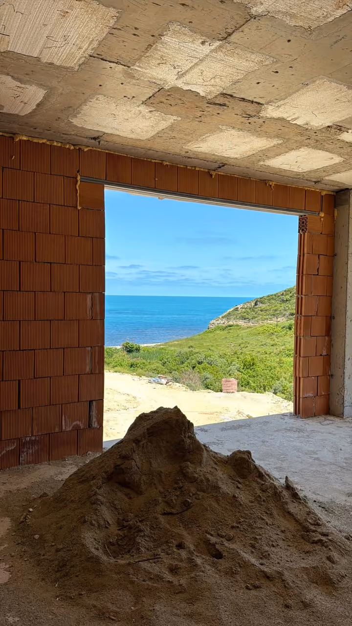 An unfinished brickwork room with construction materials and an opening toward the sea. Undated photograph supplied in the construction source folder; it does not establish the current completion status.