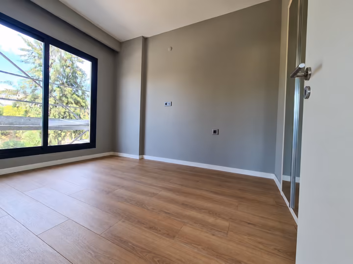 Photograph of an empty room with wood flooring and a large window.
