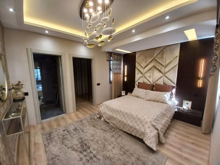A furnished show apartment bedroom with a padded wall and mirrored wardrobe.
