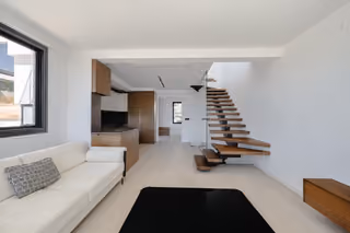 Living room with an open kitchen and wooden staircase behind glass balustrades.