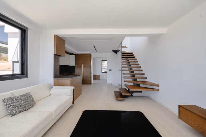 Living room with an open kitchen and wooden staircase behind glass balustrades.