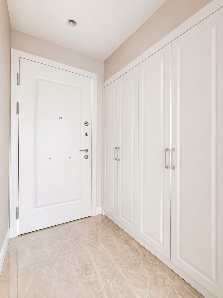 Apartment entrance with white fitted storage cabinets and tiled flooring.