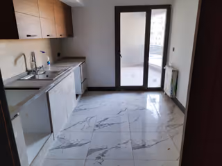Photograph of the kitchen cabinets, sink, tiled floor and glazed door to the balcony.
