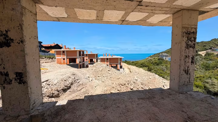 An unfinished villa interior overlooking nearby construction, vegetation and the sea. Undated photograph supplied in the construction source folder; it does not establish the current completion status.