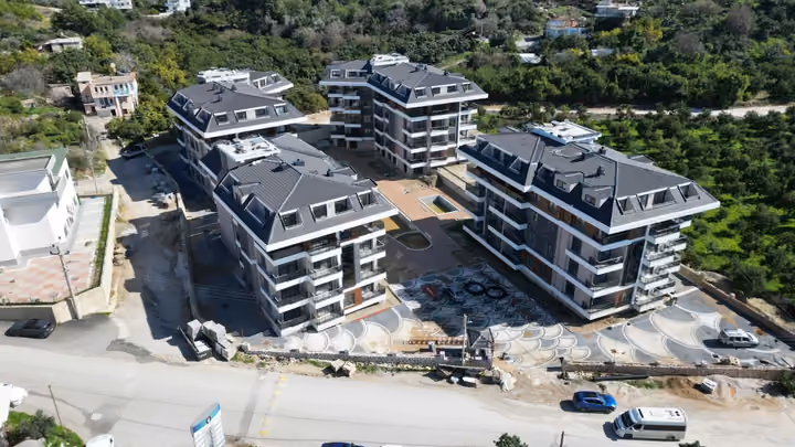 Exterior photograph of four blocks and courtyard work in Oba Alanya in February 2026