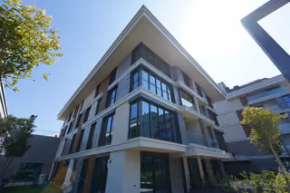 An upward view of a glazed corner facade with terraces and surrounding planting.