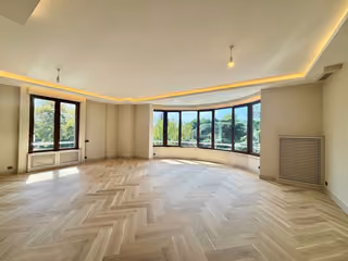 Alternate view of the living room, broad windows and herringbone-pattern flooring.