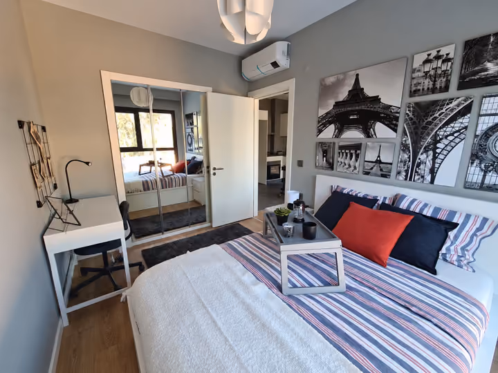 Photograph of a furnished bedroom with a bed and a desk beside the window.
