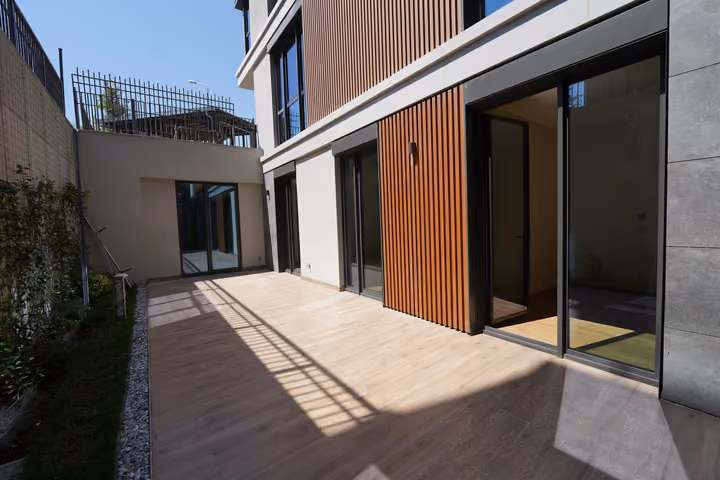 Photograph of a lower-level terrace beside glazed doors and timber-effect facade panels in Zekeriyakoy.