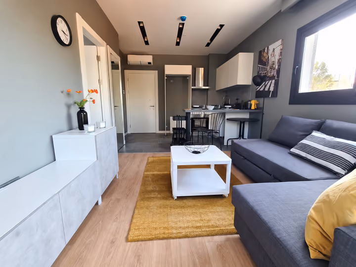 Photograph of a furnished sitting area connected to an open kitchen and breakfast counter.