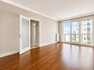 Living room with wood flooring, large windows and an open door to the hallway.