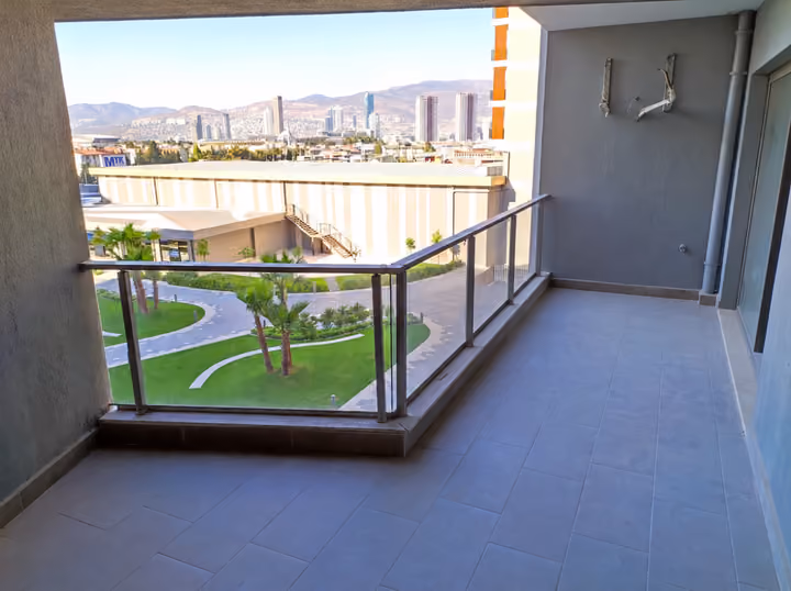 Photograph from a tiled balcony with glass railing overlooking the shared grounds, nearby buildings and distant hills.