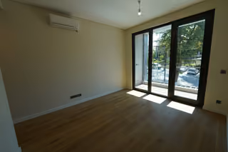 A wide view of the unfurnished living room with glazed balcony doors and air conditioning.