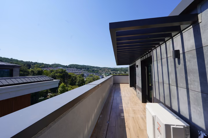The long terrace beside the glazed facade, with wooded hills visible in the distance.