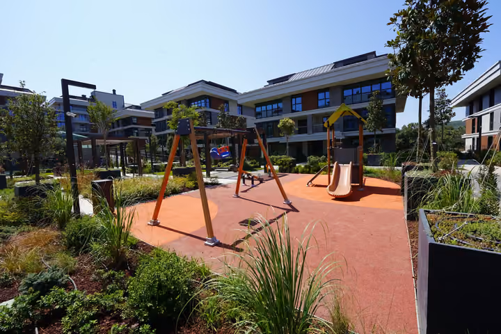 Wide view of the playground with a swing frame, slide and landscaped paths.