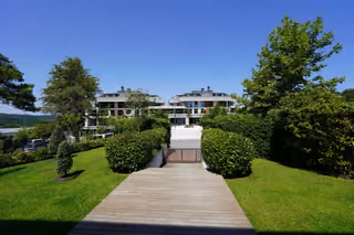 A timber-finished walkway between trimmed hedges and lawns leading toward the buildings.