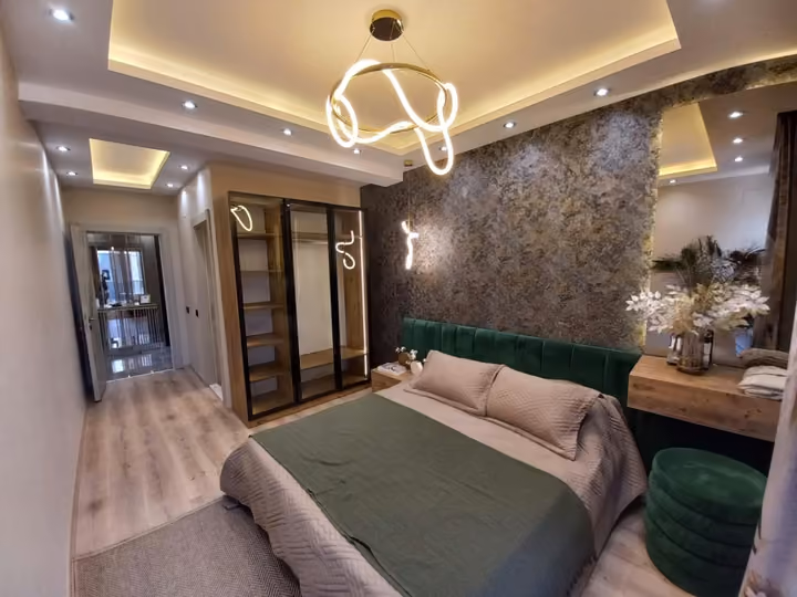A show apartment double bedroom with an upholstered headboard and green armchair.