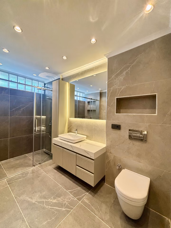 Bathroom with a glass shower enclosure, countertop basin and wall-mounted toilet.