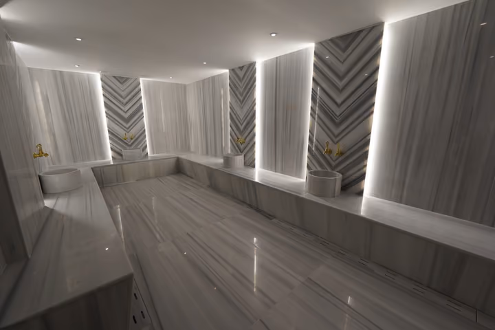 Wide view of the hammam's stone surfaces, washing basins and illuminated wall panels.