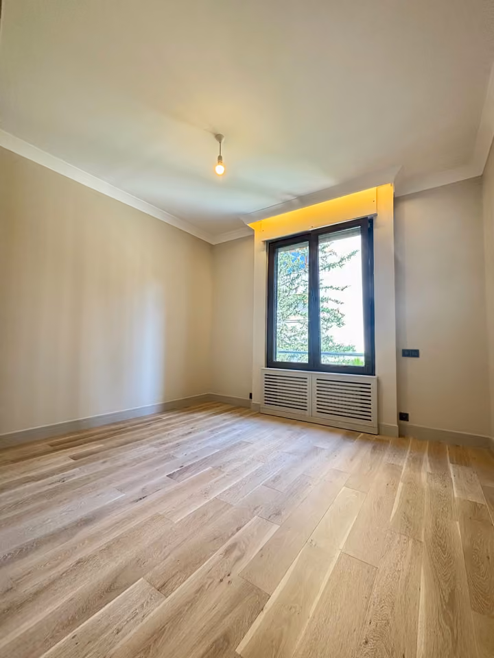 Bedroom with wood-look flooring and a window facing trees.