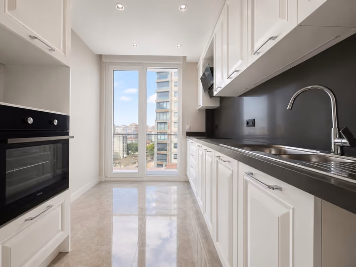 Narrow kitchen with white cabinetry, a built-in oven and a full-height window.