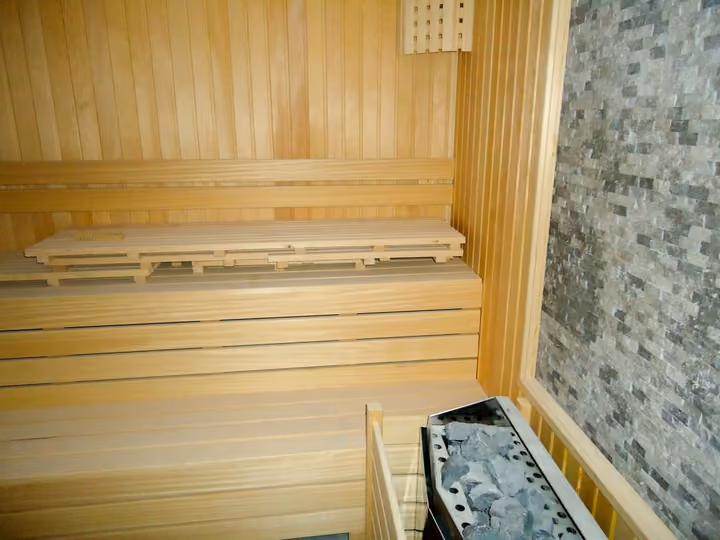 Timber sauna with tiered seating and a sauna heater.