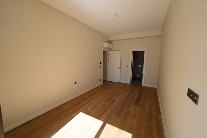 A wide view of the bedroom showing the hall door, bathroom entrance and wall-mounted air conditioning.