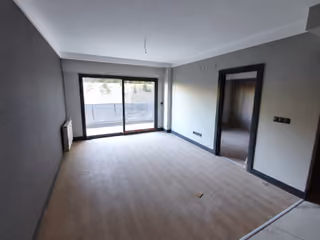 Photograph of an unfurnished living room with wood-look flooring and glazed access to a balcony.