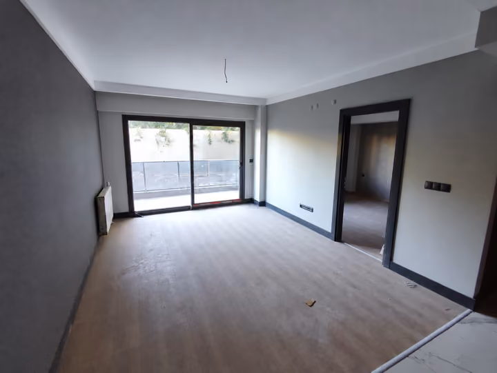 Photograph of an unfurnished living room with wood-look flooring and glazed access to a balcony.
