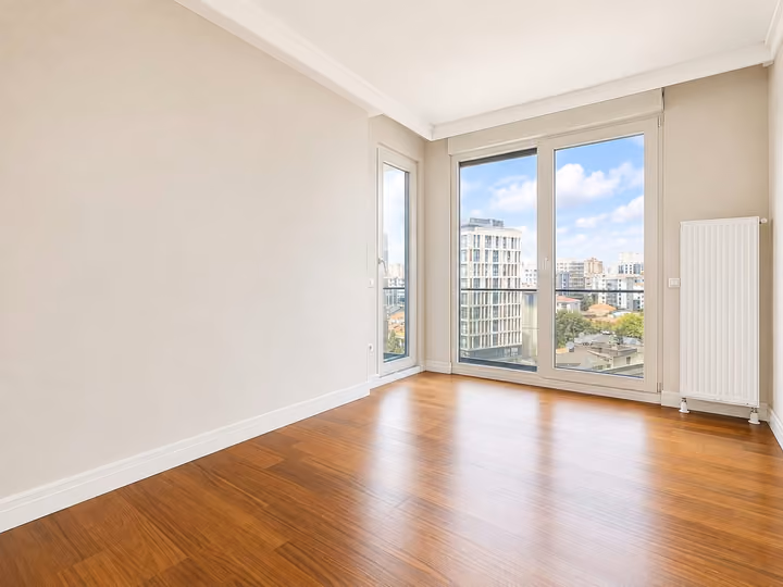 Empty bedroom with wood flooring, corner windows and a city view.