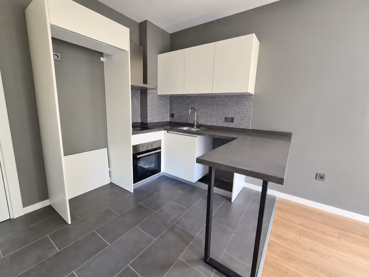 Photograph of an open kitchen with white cabinets, a worktop and fitted appliances.