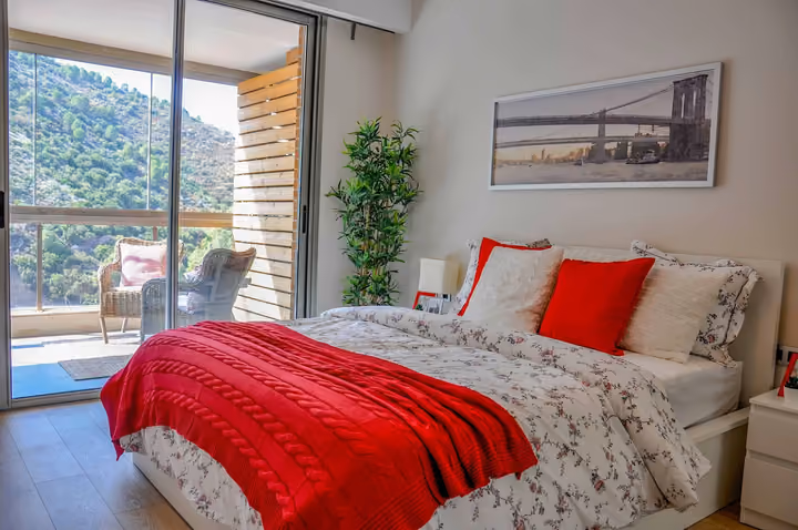 Bedroom with a balcony facing green hills.