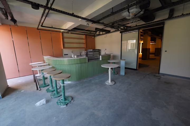 Interior with a curved counter and stools, with protective wrapping and finishing materials still visible. Source photograph dated 22 July 2026.