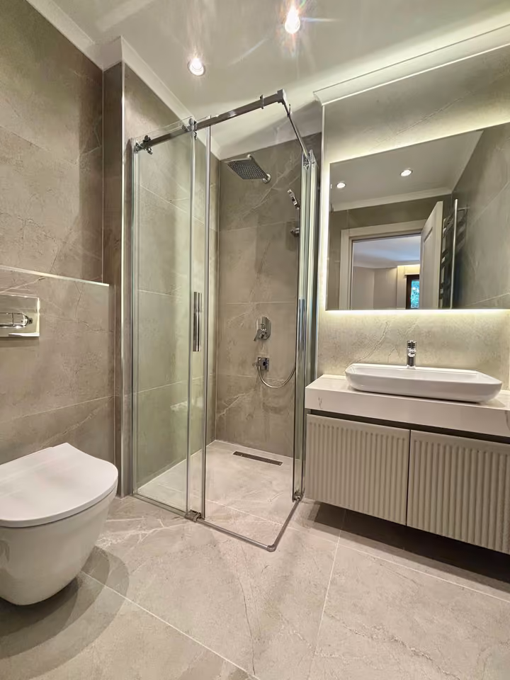 Bathroom with a glass shower enclosure, illuminated mirror and countertop basin.