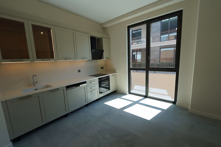 Photograph showing fitted kitchen cabinets, appliances, tiled flooring and a large glazed external door in Zekeriyakoy.
